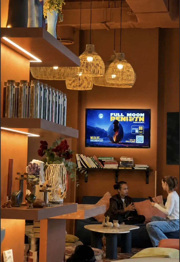 Digital signage screen in a café interior showing promotional content on a wall-mounted display in a modern lounge environment